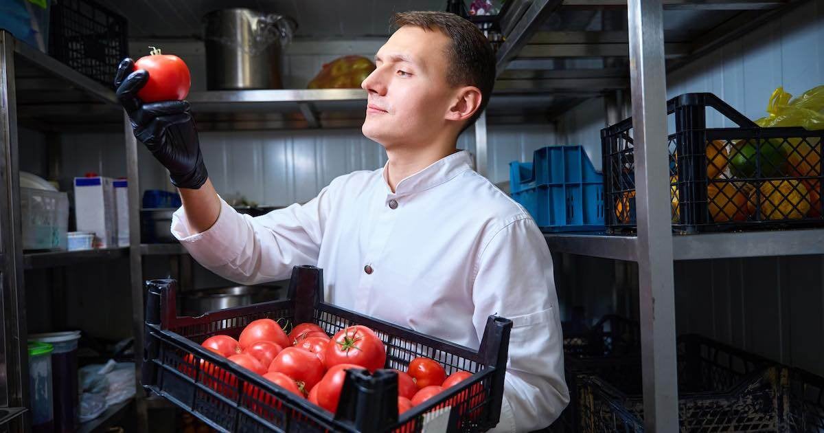 guy examining a tomato in a walk-n refrigerator