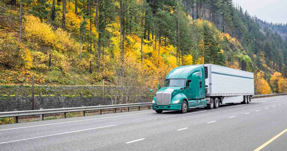 truck driving on the highway with evergreen trees in the background