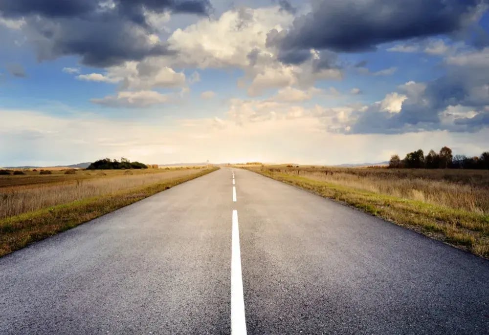 Empty two-lane highway running through open grassland under a cloudy sky.
