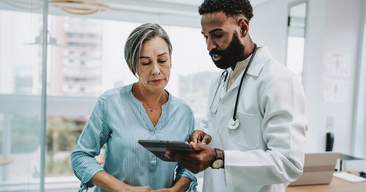 A doctor shows a tablet to a patient in a clinic office.